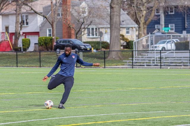 Coach Roy Shaba striking a soccer ball on the field