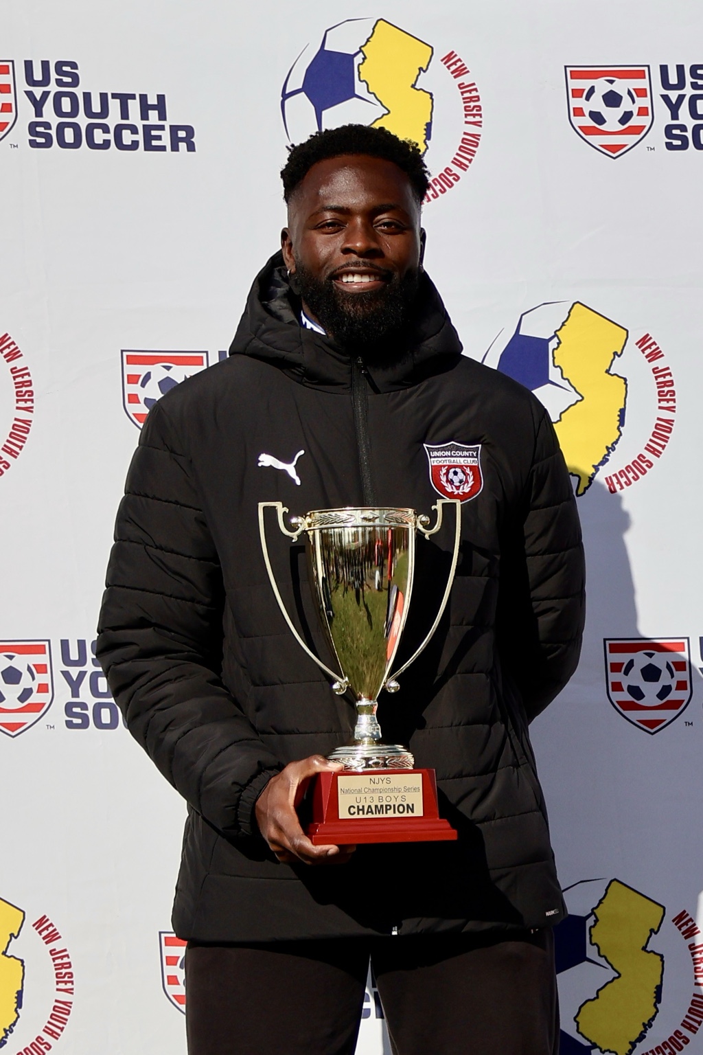 Roy Shaba, Founder and Head Coach, holding a soccer championship trophy